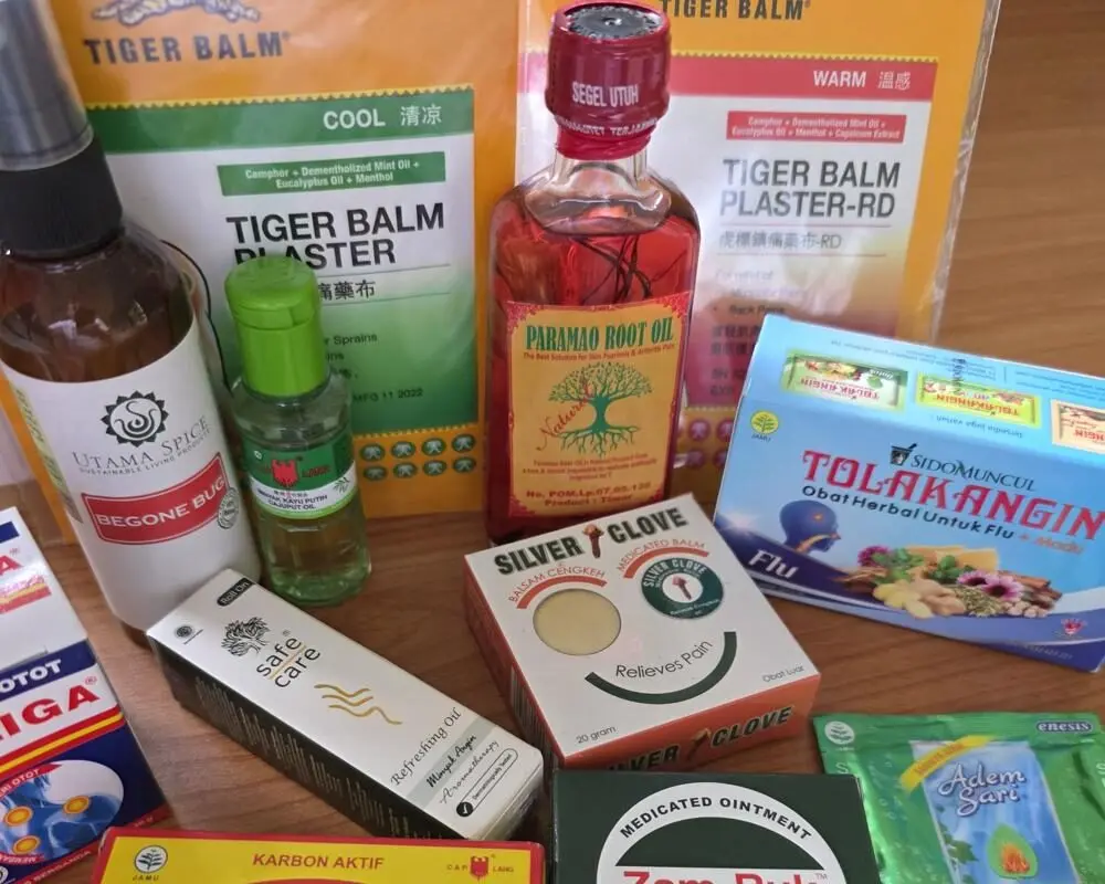 A collection of common medicines to buy in Bali, including Tolak Angin, Tiger Balm, Paramao Root Oil, and Safe Care aromatherapy oil, all available at a local apotek.