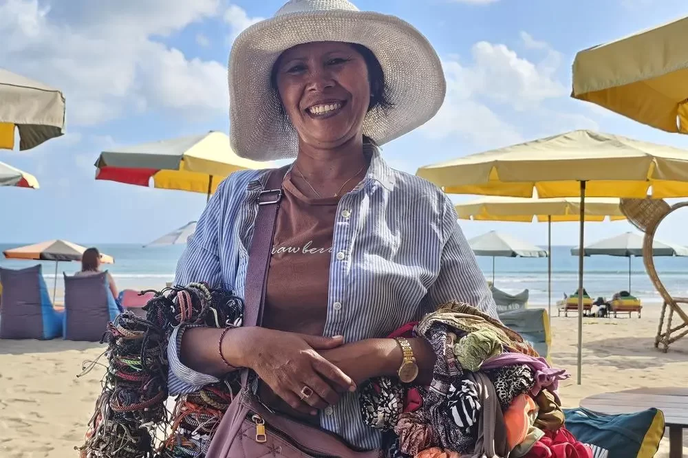 A portrait of a smiling Balinese beach seller named Angela Cindy on Legian beach, her arms full of colorful bracelets, representing the local people of Bali.