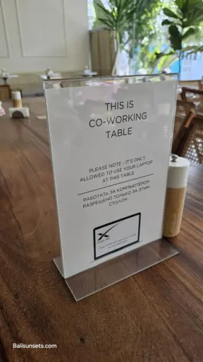 A sign on a wooden cafe table that reads "THIS IS CO-WORKING TABLE" with a note about a new Starlink internet connection, symbolizing the rise of digital nomads in Bali.