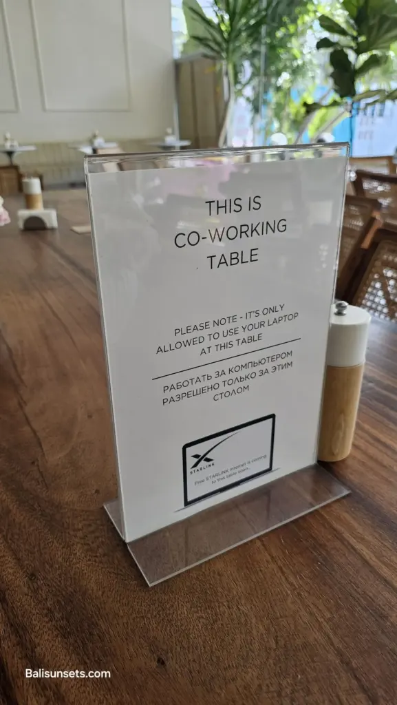 A sign on a wooden cafe table that reads "THIS IS CO-WORKING TABLE" with a note about a new Starlink internet connection, symbolizing the rise of digital nomads in Bali.